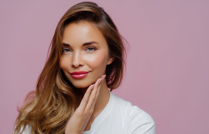 Famosas con bichectomía: una mujer caucásica de ojos claros acaricia su rostro mientras sonríe, mostrando los resultados positivos de un procedimiento estético
