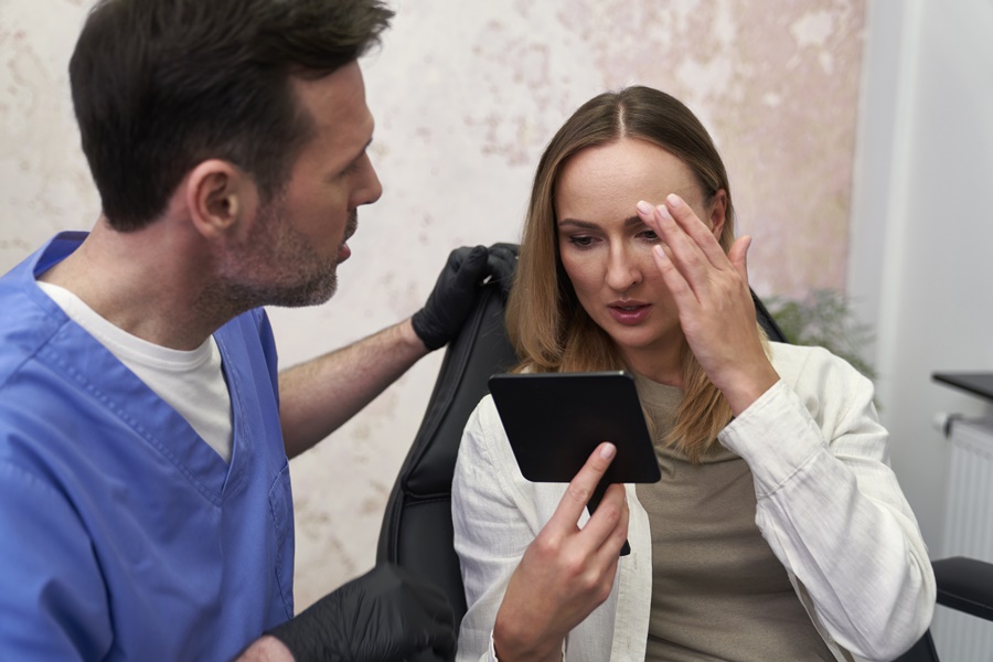 Mujer analizando su rostro frente al espejo durante una consulta médica, antes de decidir sobre procedimientos faciales combinados.
