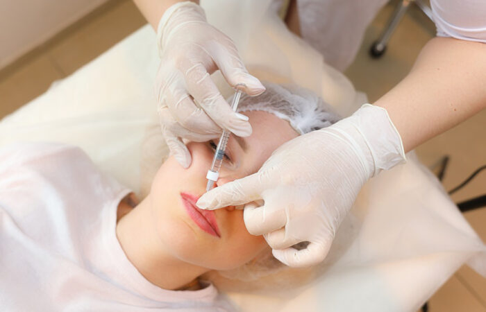 Mujer recostada recibiendo una inyección de ácido hialurónico en la zona de los labios, procedimiento estético para mejorar volumen y observar efectos inmediatos en el rostro.