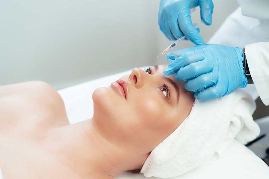 Aplicación de ácido hialurónico en la frente de una mujer por parte de un especialista, destacando los efectos rejuvenecedores y la precisión del tratamiento facial.