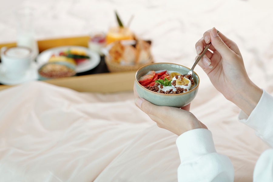 Persona desayunando yogur con frutas y cereales integrales en cama, muestra de alimentación postoperatorio cirugía estética rica en nutrientes para la cicatrización.