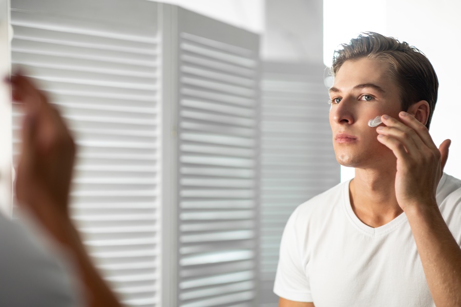 Hombre aplicando crema hidratante frente al espejo, cuidando su piel. Representa el hábito de hidratar la piel a diario para prevenir el envejecimiento prematuro de la piel.