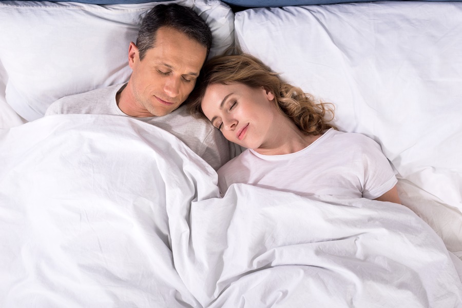 Pareja durmiendo plácidamente en una cama blanca, simbolizando el descanso nocturno. Imagen vinculada al sueño reparador como factor clave para prevenir el envejecimiento prematuro de la piel.