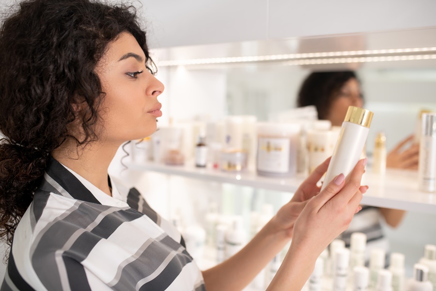 Mujer observando un envase cosmético con atención en una tienda. Imagen vinculada al uso consciente de cosméticos para prevenir el envejecimiento prematuro de la piel.