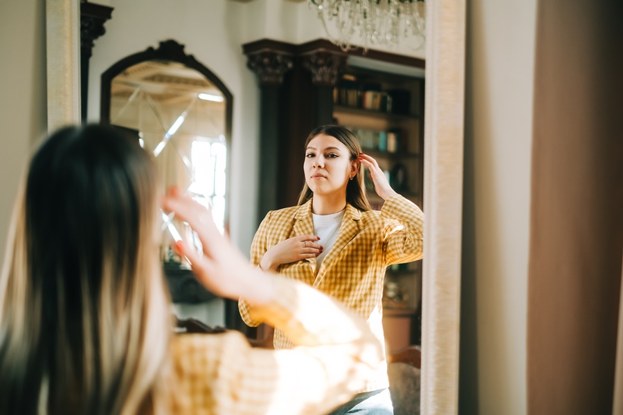 Mujer con expresión segura observando su imagen en el espejo, simbolizando el proceso de aceptación personal y el manejo de expectativas ante una cirugía plástica.