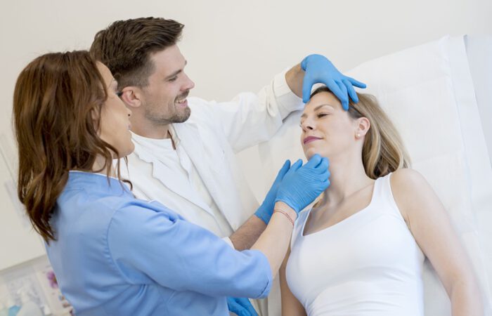 Médico y asistente evaluando el rostro de una paciente durante una consulta para cirugía estética, considerando los factores hormonales y su impacto en el resultado final.