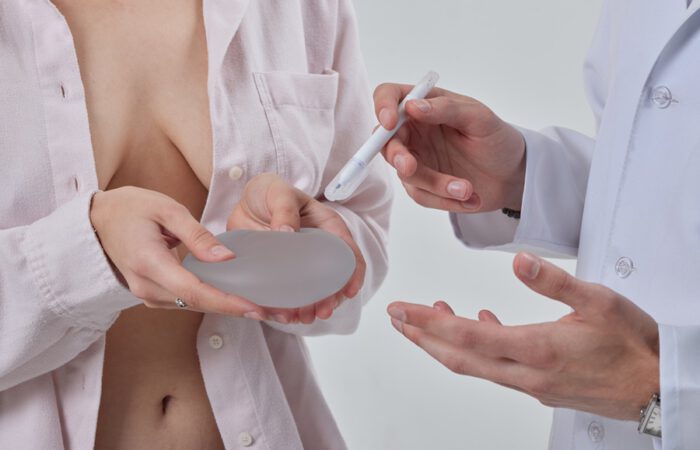 Paciente sosteniendo prótesis mamaria durante consulta médica, en evaluación para mastopexia con o sin prótesis, mientras el cirujano explica el procedimiento y sus opciones.