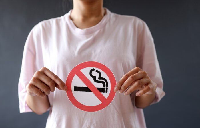 Mujer sujetando un cartel de prohibido fumar sobre su pecho, simbolizando la importancia de evitar el tabaco antes de una cirugía estética. Concepto visual de “tabaco y cirugía estética” enfocado en la prevención.