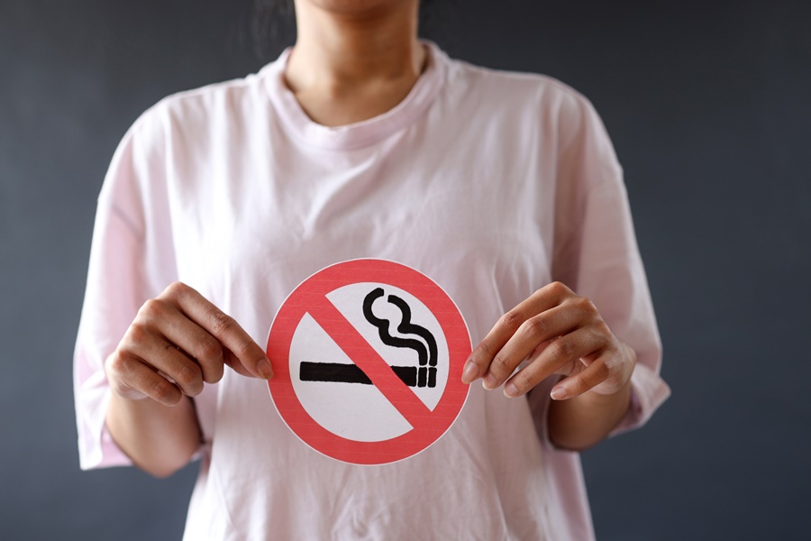 Mujer sujetando un cartel de prohibido fumar sobre su pecho, simbolizando la importancia de evitar el tabaco antes de una cirugía estética. Concepto visual de “tabaco y cirugía estética” enfocado en la prevención.