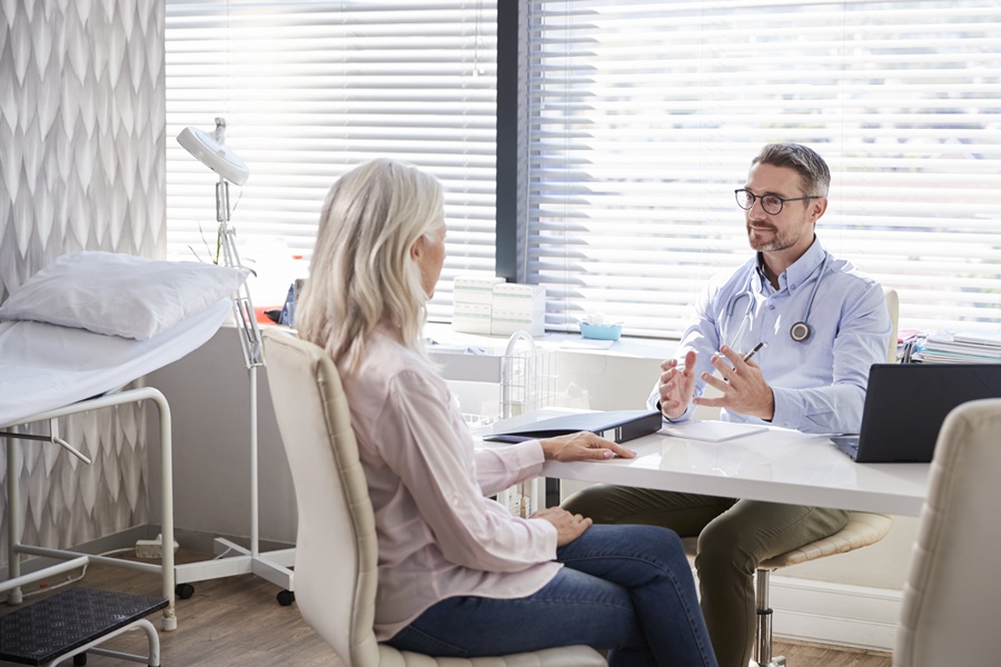 Paciente adulta en consulta médica con un cirujano estético. Ambos conversan en un entorno clínico sobre los efectos del tabaco y cirugía estética antes de una posible intervención.