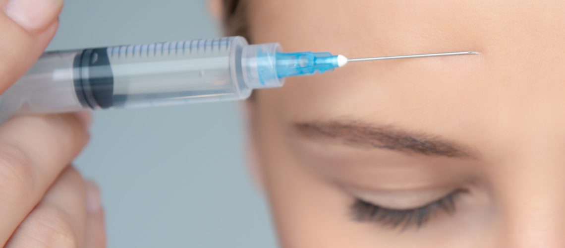 Closeup Photo of a Women's Face Part with Syringe near Forehead over Gray Background. Forehead Wrinkle Smoothing. Nice Female in a Beauty Clinic.